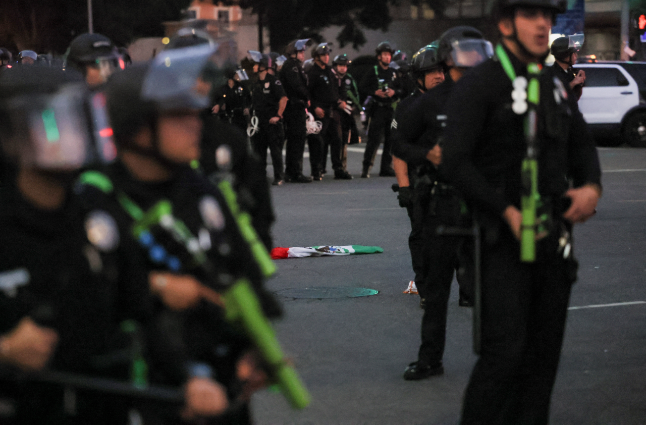 A Mexican flag lies on the ground among law enforcement deployed to contain protests against federal immigration raids in downtown Los Angeles. (Фото: REUTERS/Leah Millis)